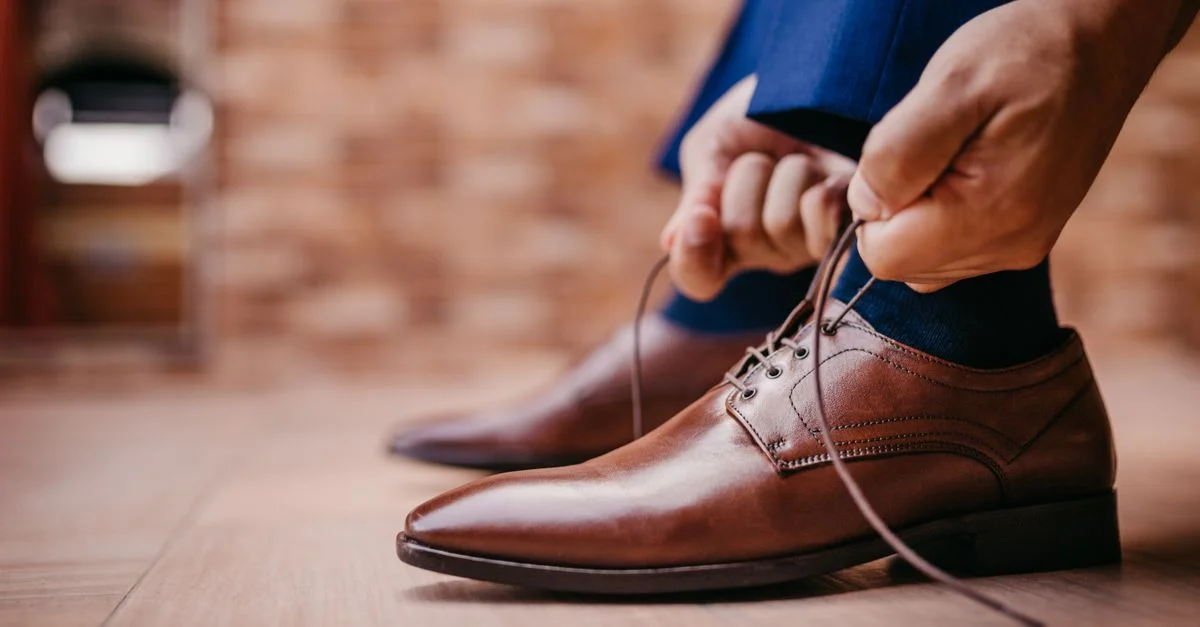 Primer plano de un hombre atando los cordones de unos elegantes zapatos de cuero marrón en interiores.