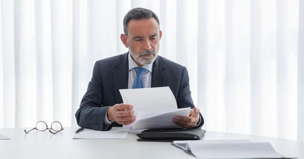 Hombre de negocios mayor concentrado en leer documentos en una mesa en un brillante entorno de oficina.