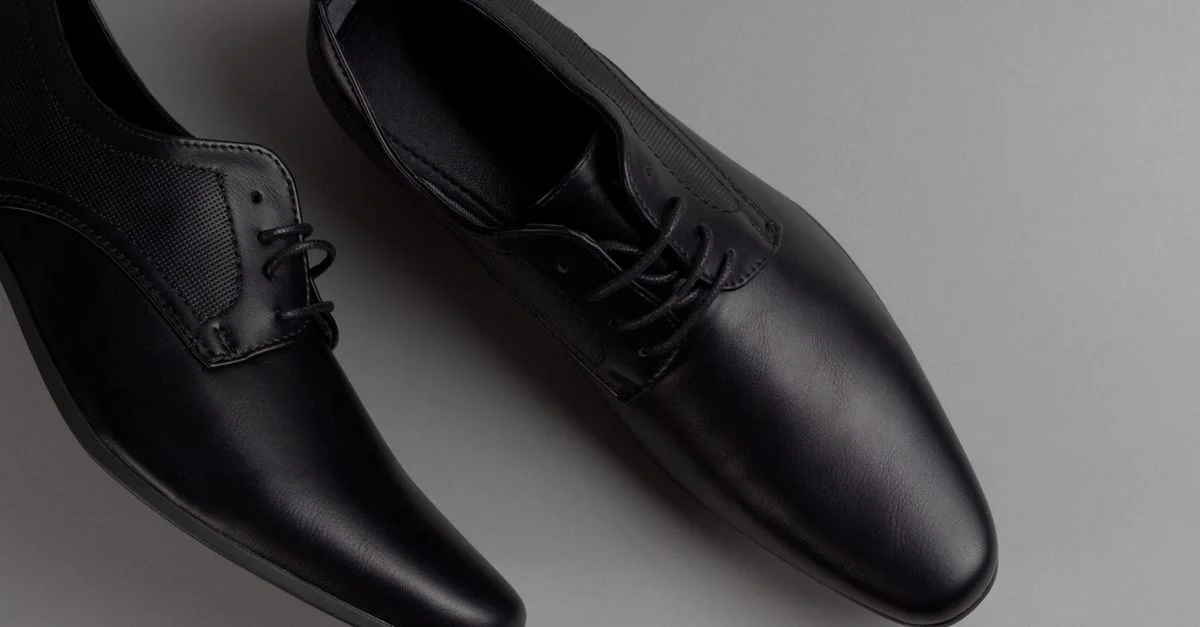 Par de zapatos formales negros elegantes mostrados sobre un fondo gris minimalista, perfectos para atuendo de negocios.